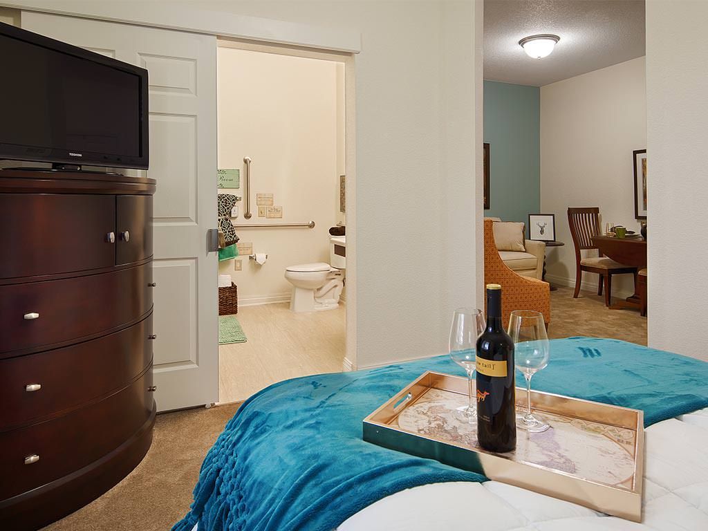 A cozy bedroom with a wine bottle and glasses on a tray, featuring an open view of the bathroom and dining area.