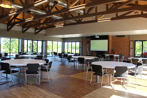 A spacious event space featuring round tables and chairs, large windows that provide natural light, and a projector screen for presentations.