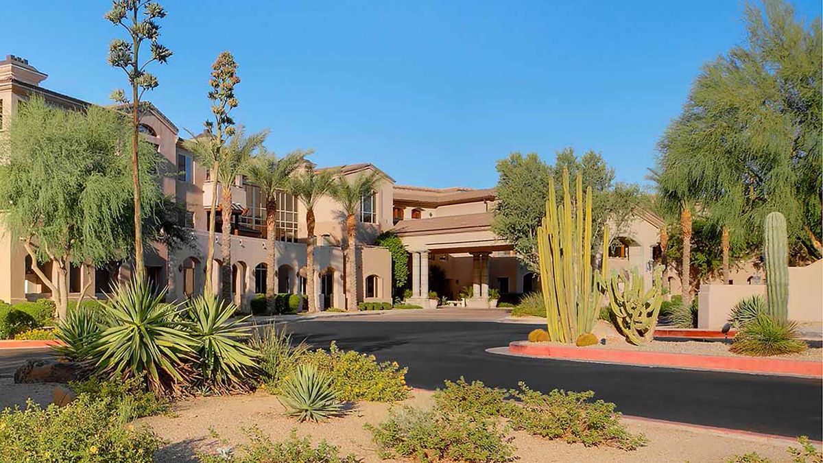 A desert landscape featuring a large building surrounded by cacti and palm trees.