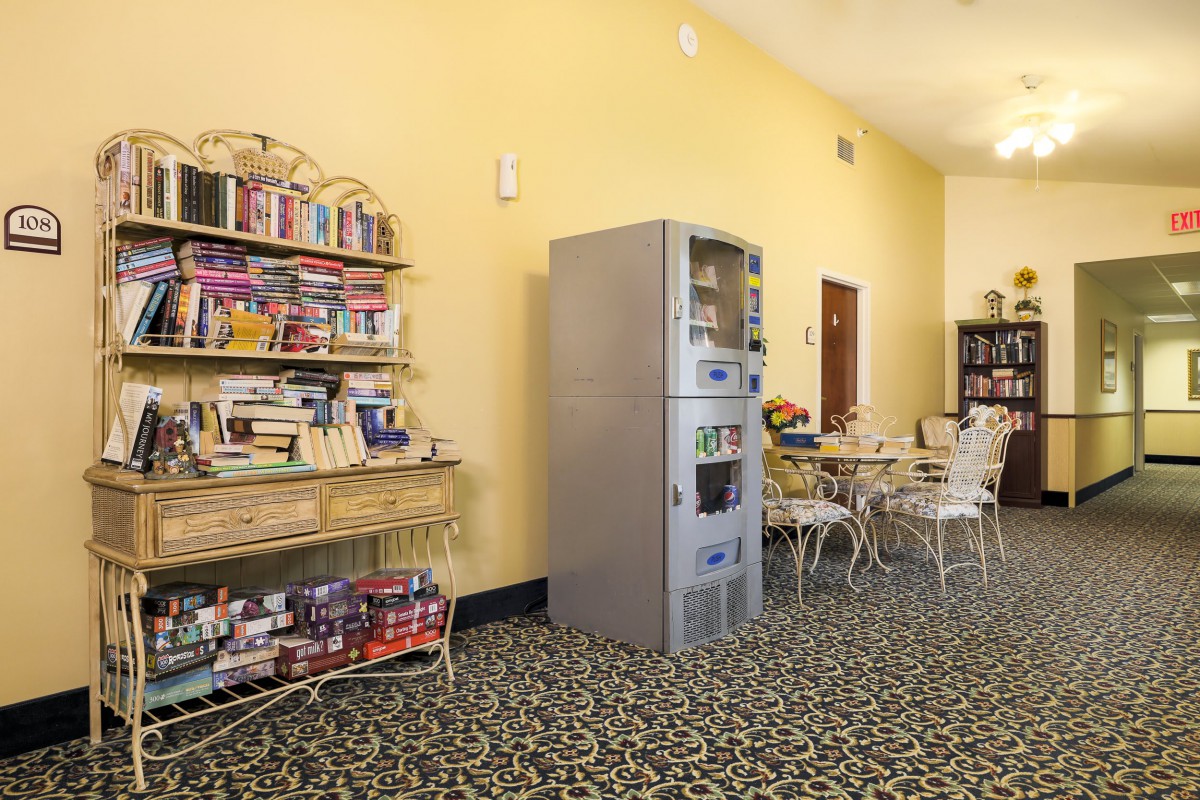 A cozy room with a vending machine, bookshelf, and a small seating area.