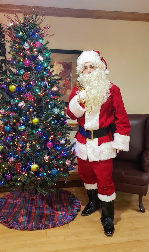 A festive Santa Claus stands beside a beautifully decorated Christmas tree.