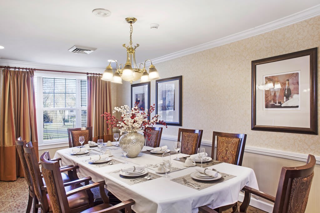 An elegantly set dining room with a large table, surrounded by chairs and illuminated by a chandelier.
