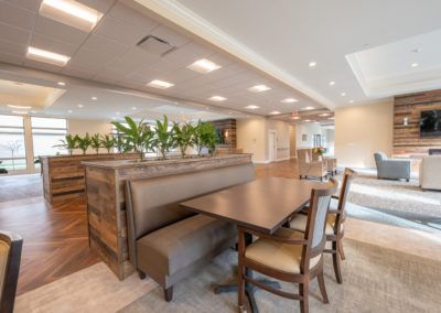 A modern restaurant interior with a spacious dining area, featuring wooden tables, chairs, and decorative plants.