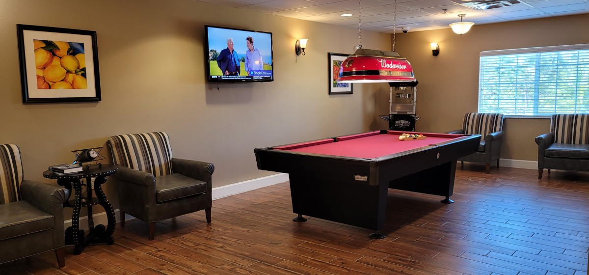 A cozy game room with a pool table, wall-mounted TV, and comfortable armchair.
