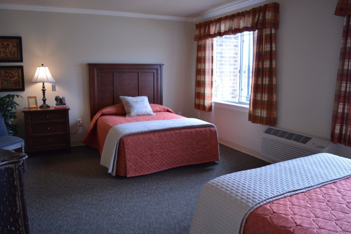 A neatly arranged hotel room featuring two beds with matching bedspreads and a large window with curtains.