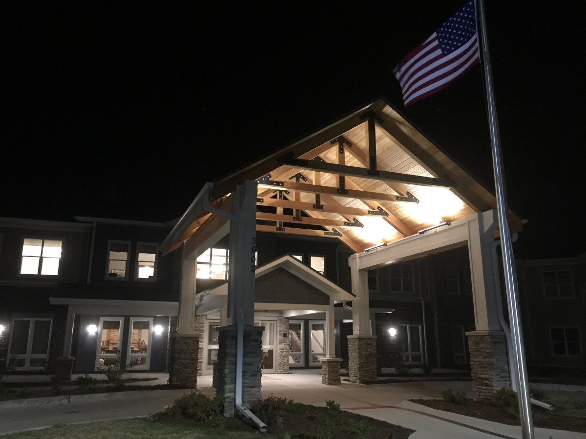 An illuminated building entrance at night with an American flag waving in the foreground.