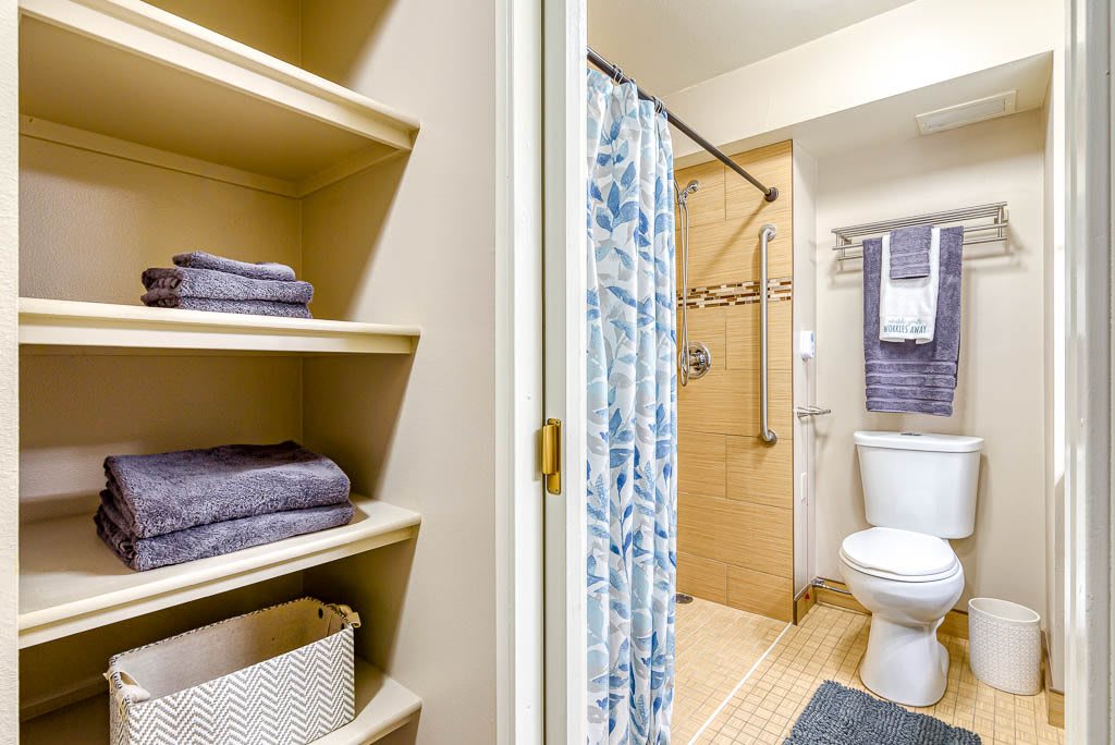 A bathroom with organized shelves, a shower curtain, and neatly placed towels.