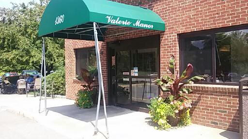 Entrance of a building with a green awning and decorative plants.
