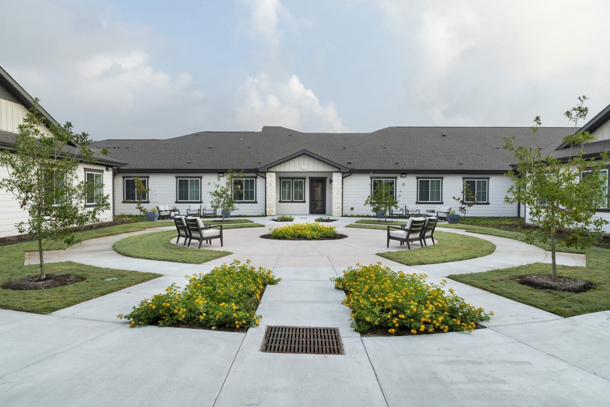 A symmetrical garden with benches and pathways leading to a building under a cloudy sky.