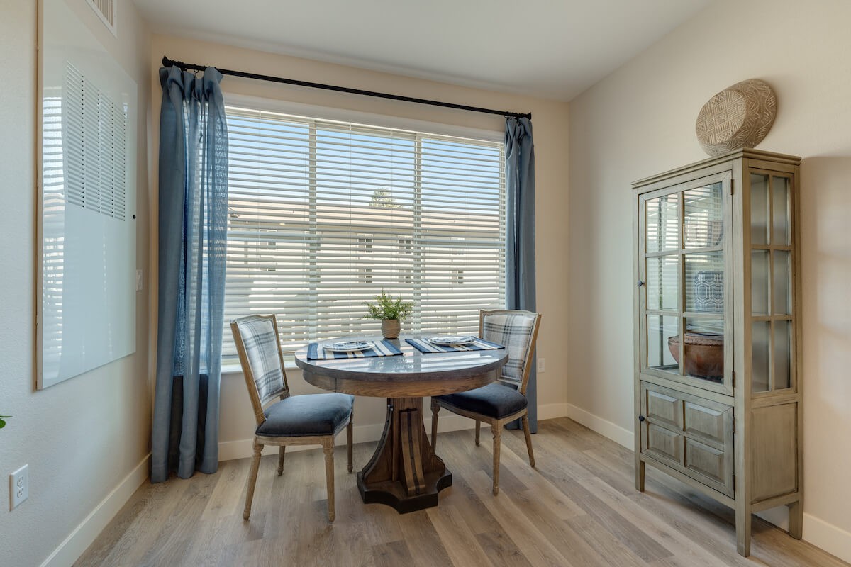 A cozy dining area with a round table and two chairs by a large window letting in natural light.