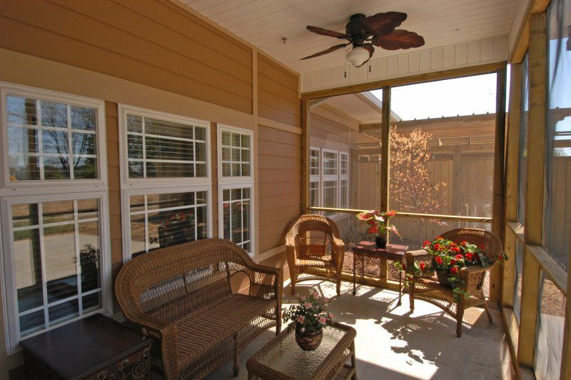 A cozy outdoor patio with wicker furniture and plants, well-lit by natural sunlight.