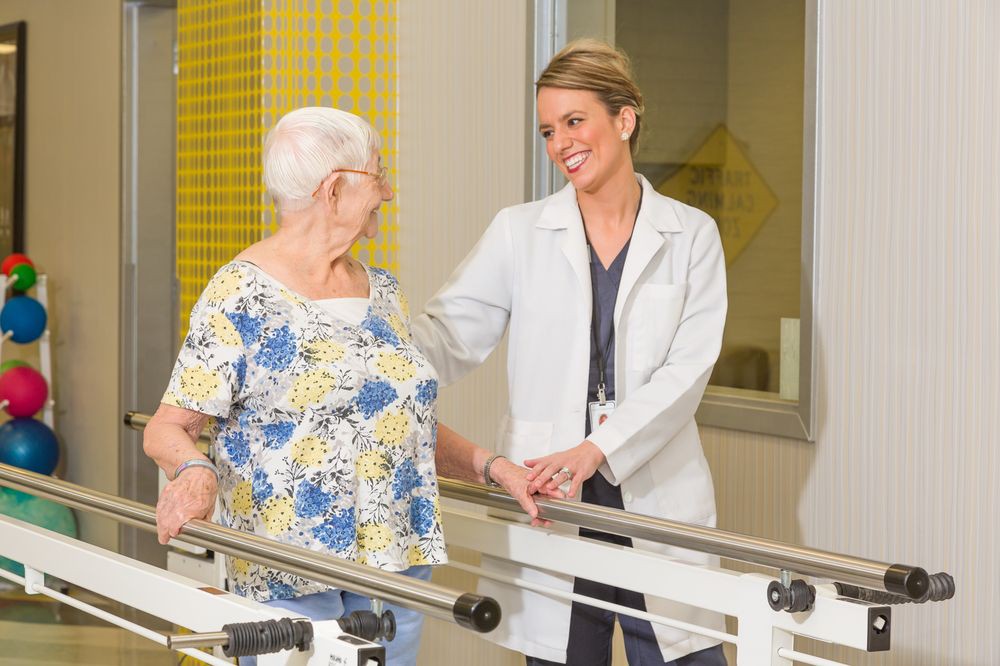 A healthcare professional assists an elderly woman with physical therapy exercises.