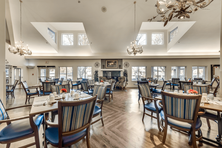A spacious dining area with elegant furniture and chandeliers, featuring large windows and wood flooring.