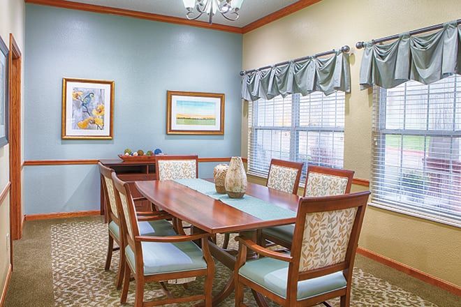 A well-furnished dining room with a wooden table, chairs, decorative artwork, and natural light from the window.