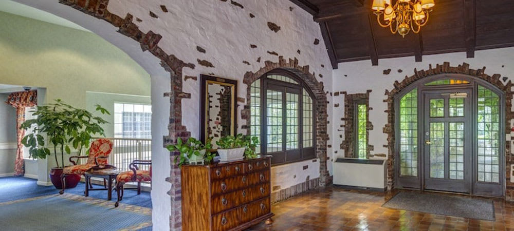 A charming interior with rustic brickwork and arched windows, complemented by wooden furniture and greenery.