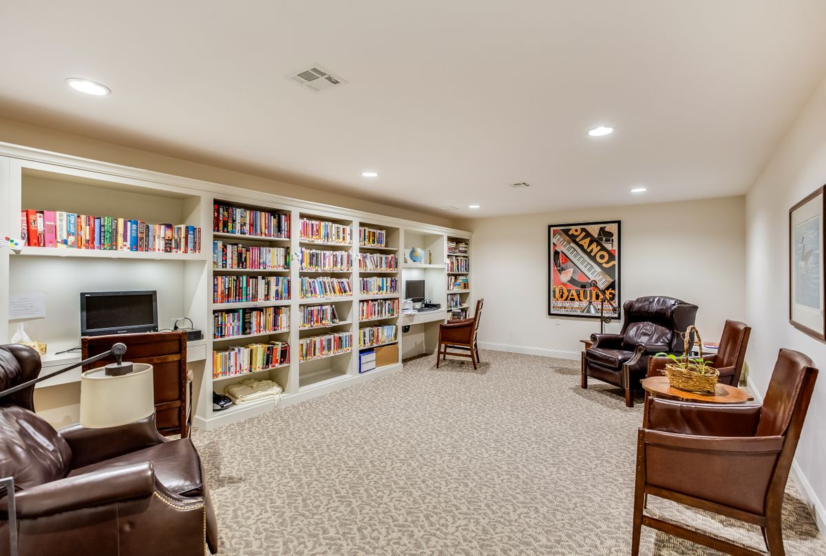 A cozy home library with bookshelves, armchairs, and a computer desk.