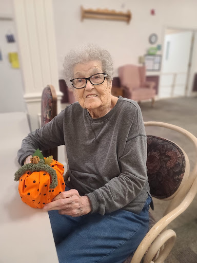 An elderly woman proudly displays her handmade orange pumpkin decoration.