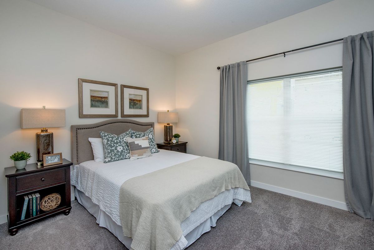 A neatly decorated bedroom featuring a bed with pillows, side tables with lamps, and a large window with curtains.