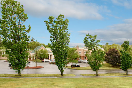 A serene view of a parking lot surrounded by trees and buildings under a partly cloudy sky.