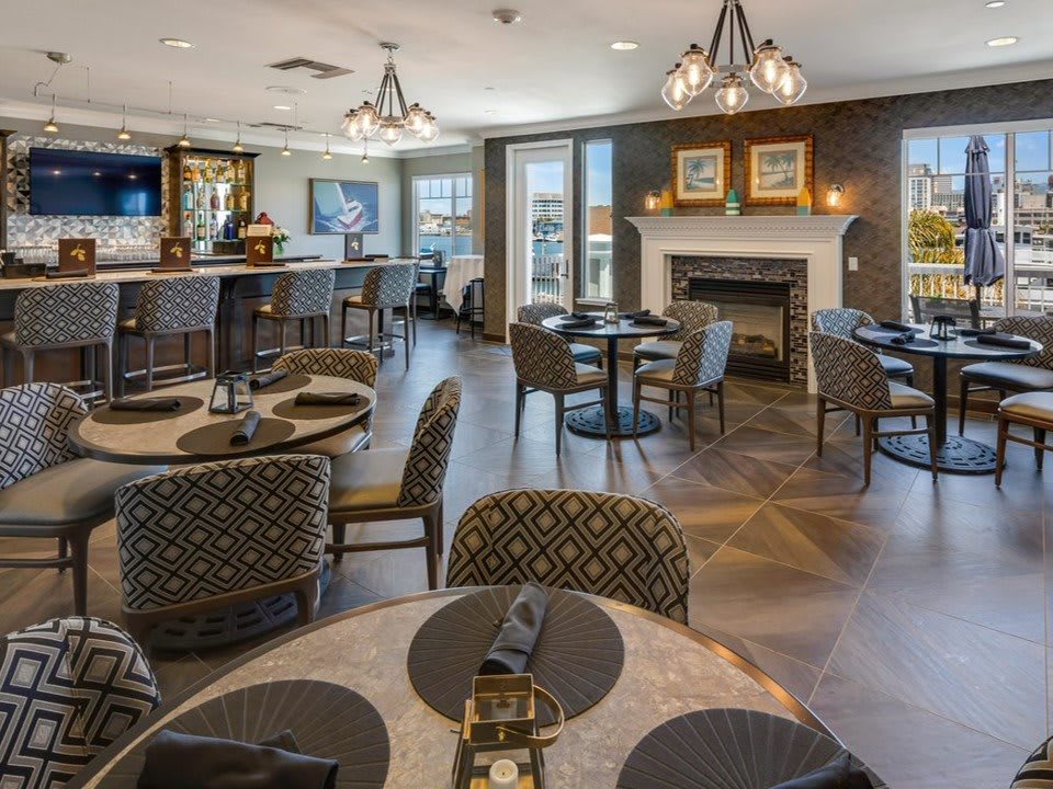 A cozy restaurant interior with a dining area featuring tables, chairs, a bar counter, and a fireplace.