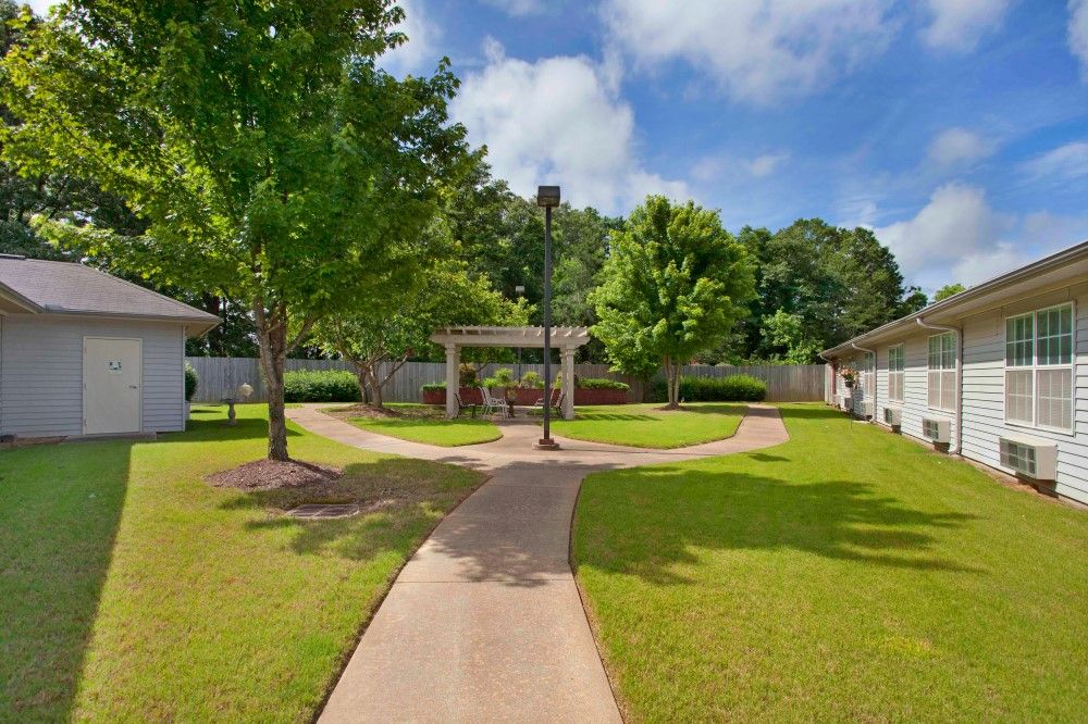 A scenic garden with a winding pathway surrounded by trees and lush greenery.