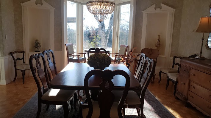 A sunlit dining room with a large table, elegant chairs, and a chandelier.