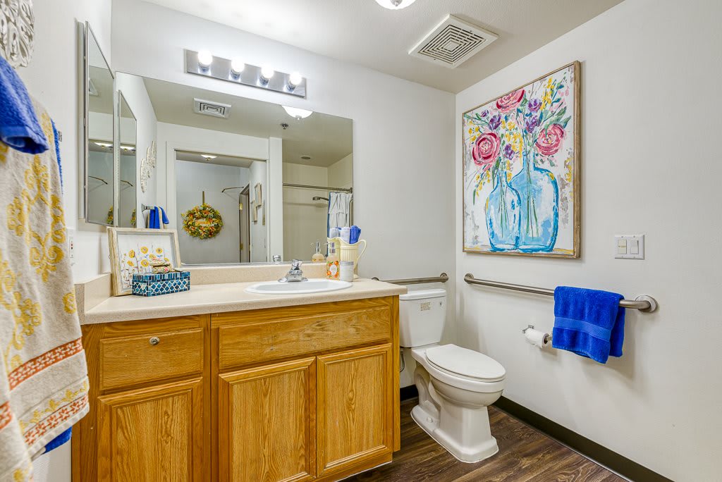 A modern bathroom featuring a wooden cabinet, large mirror, and colorful wall art.