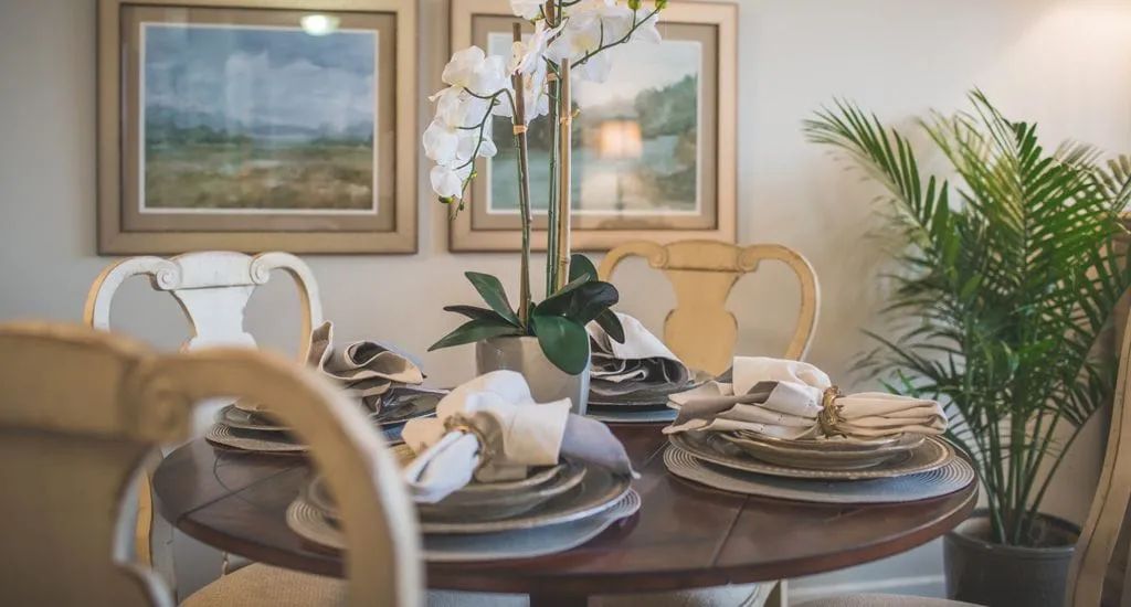 An elegantly set dining table with an orchid centerpiece and artwork in the background.