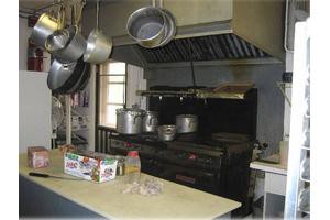 A commercial kitchen with hanging pots, a large stove, and various cooking equipment.