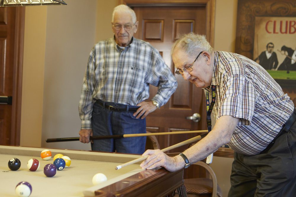 Two elderly men playing pool in a recreational setting.