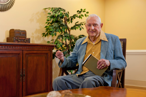 An elderly man sitting comfortably in a chair, enjoying a book in a cozy indoor setting.