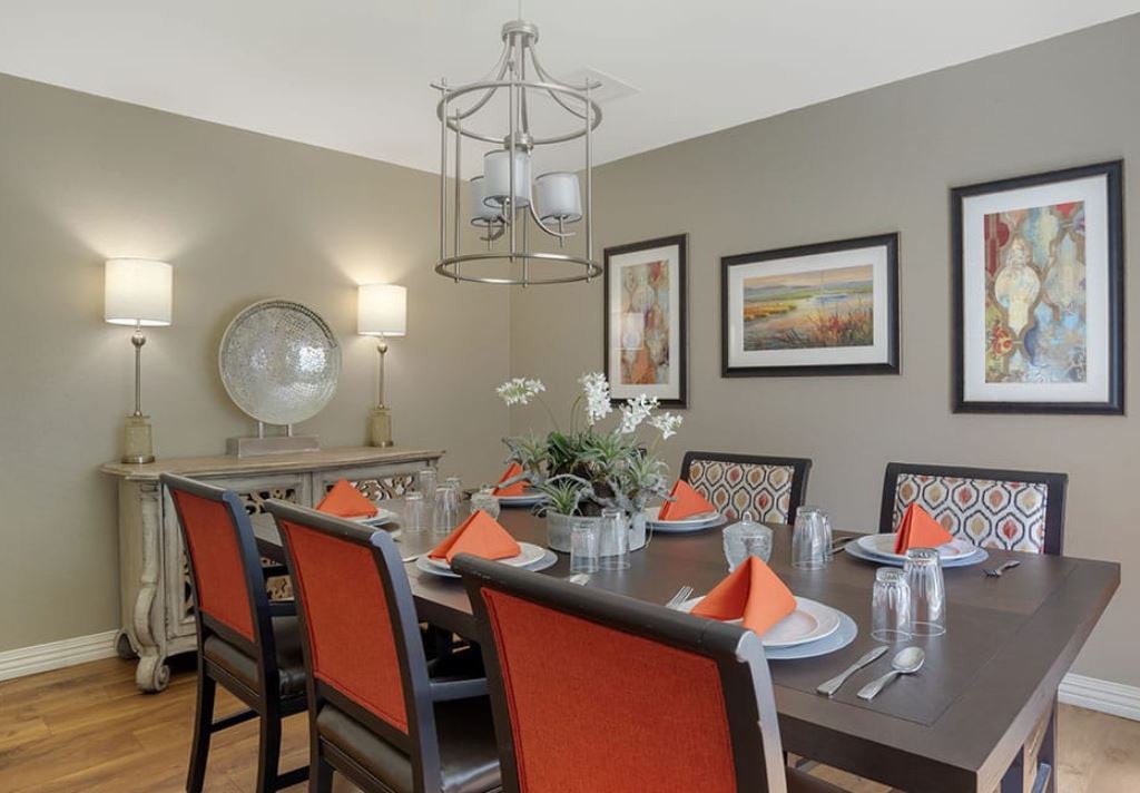 A stylish dining room with orange-accented chairs, a modern chandelier, and elegant table settings.