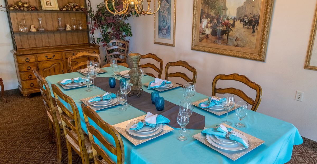 A beautifully set dining table with turquoise accents and elegant dinnerware, surrounded by wooden chairs and illuminated by a chandelier.
