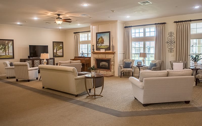 A cozy and well-decorated living room featuring a fireplace, multiple sofas, large windows with curtains, and a ceiling fan.
