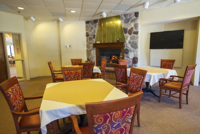 A cozy dining room with neatly arranged tables and a stone fireplace.