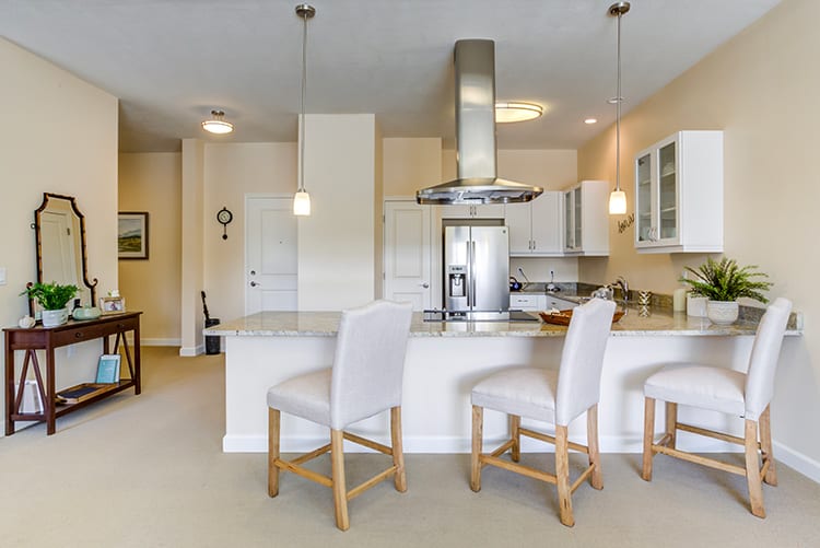 A modern kitchen with white bar stools and stainless steel appliances.