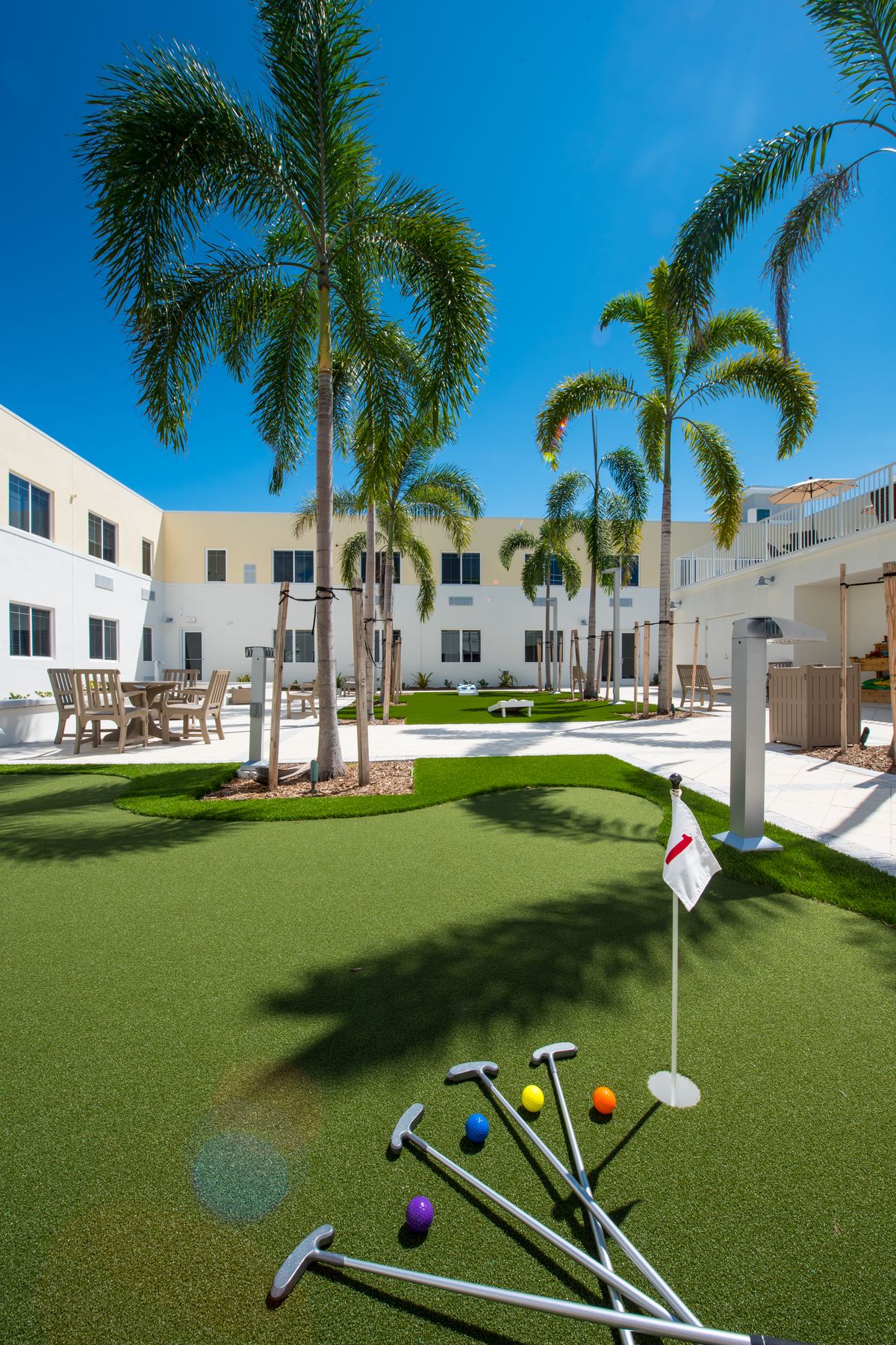 A sunny courtyard with a mini golf putting green and palm trees surrounded by a residential building.