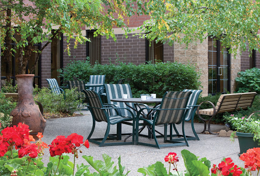 A serene outdoor seating area featuring a table surrounded by chairs, set against a backdrop of lush greenery.