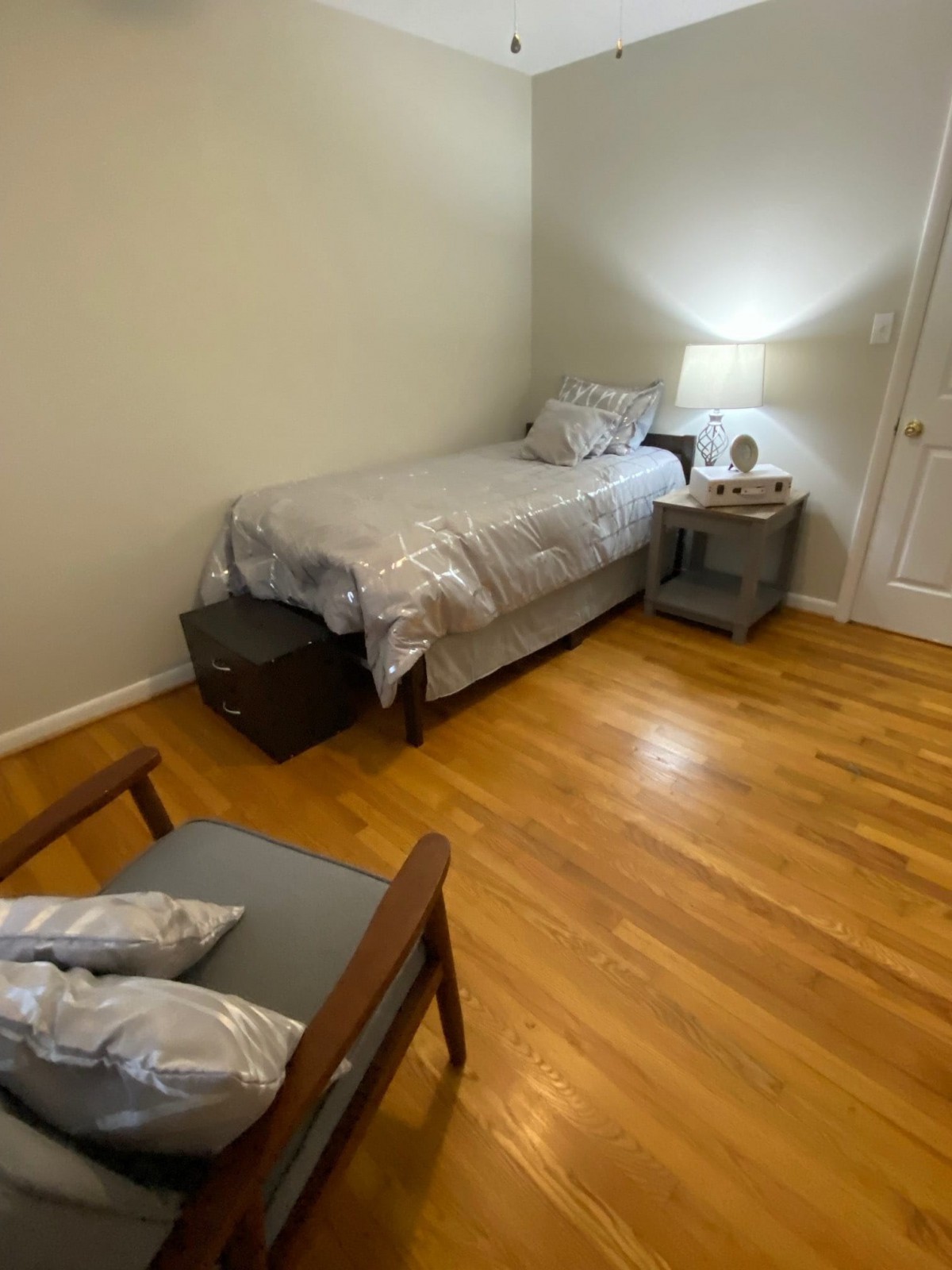 A minimalist bedroom with a single bed, nightstand, and chair on hardwood flooring.