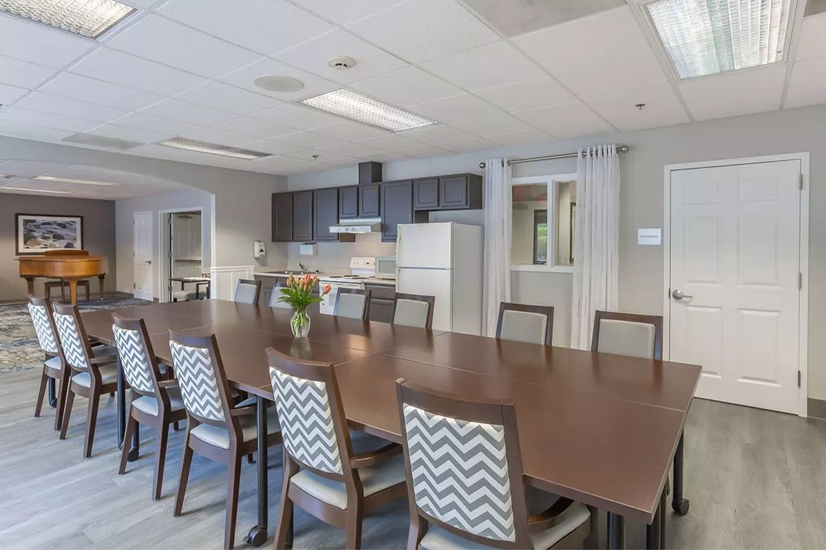 A modern conference room featuring a long table, chairs, and an adjacent kitchen area.