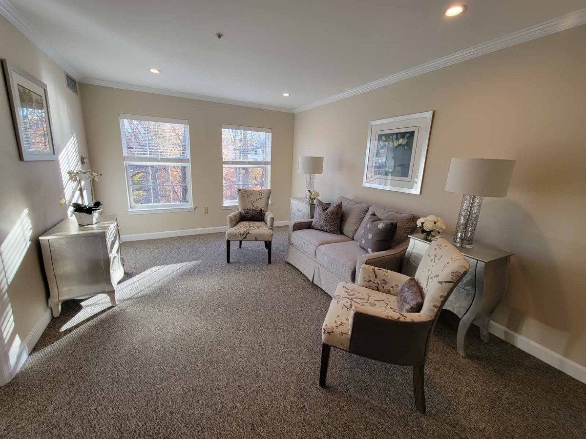 A cozy living room with a sofa, armchairs, and two large windows letting in natural light.