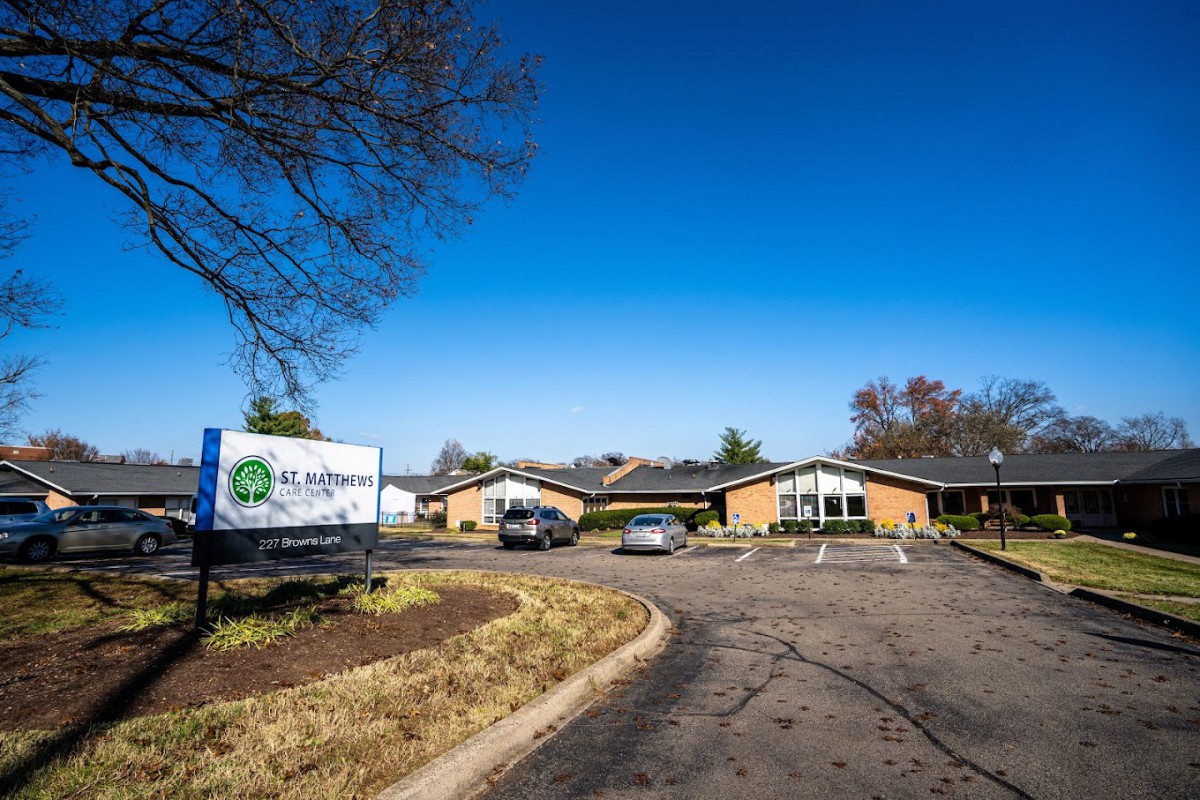 A building with a driveway, cars, and a sign under a clear blue sky.