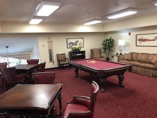 A cozy recreation room featuring a pool table and comfortable seating with red carpeting.