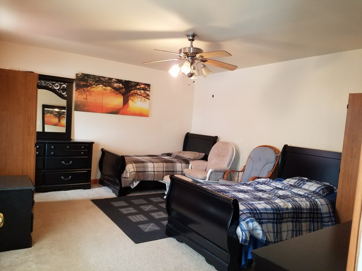 A cozy bedroom featuring twin beds, a dresser, and wall art under a ceiling fan.