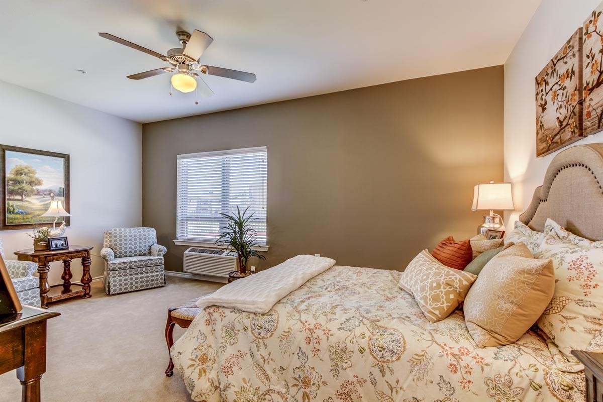 A cozy bedroom with neutral tones, featuring a bed, chair, and a large window.