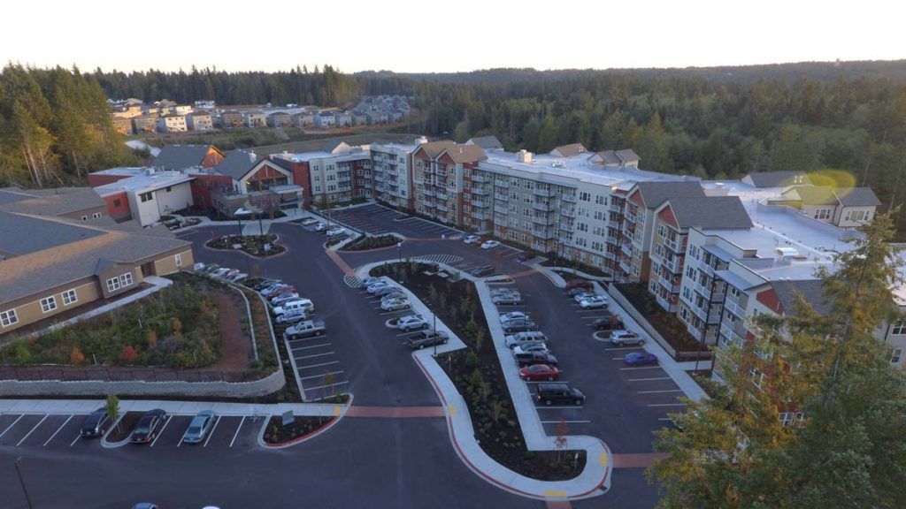 Aerial view of a large residential apartment complex with a parking lot and surrounding greenery.
