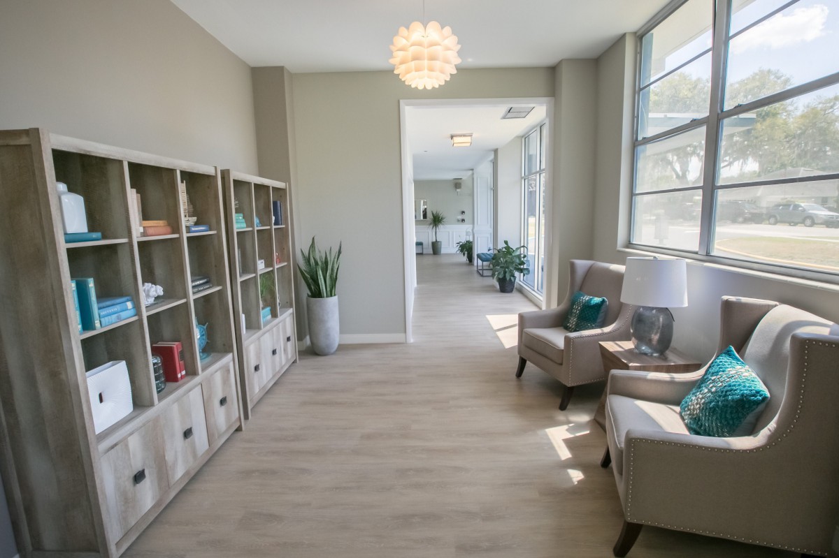 A modern waiting area with comfortable seating, bookshelves, and large windows letting in natural light.