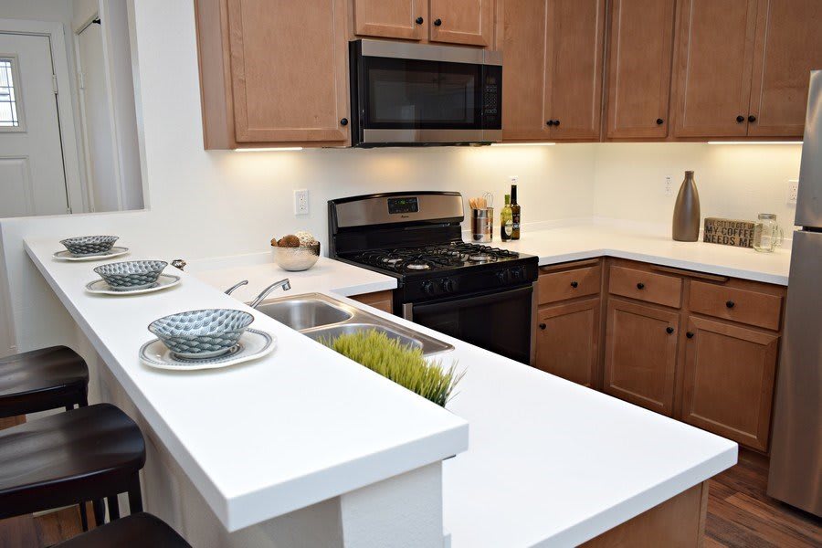 A modern kitchen with wooden cabinets, a microwave above a stove, and a white countertop with bowls.