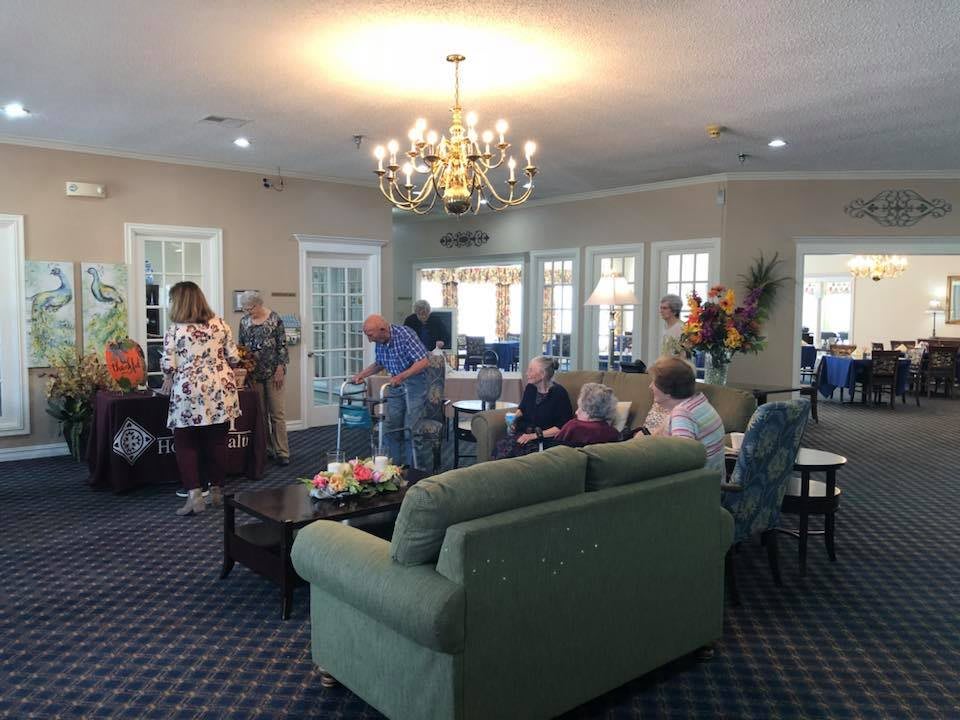 A group of people socializing in a well-lit living room with comfortable furniture and a chandelier.
