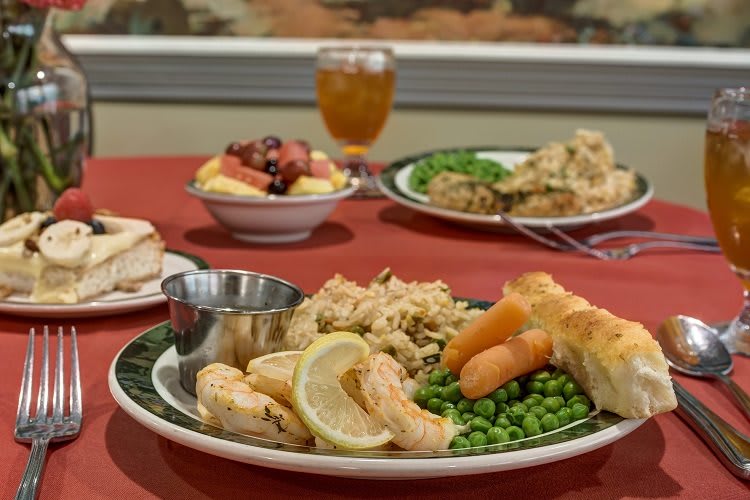 A dinner plate featuring shrimp, rice, carrots, peas, and a bread roll served at a restaurant.